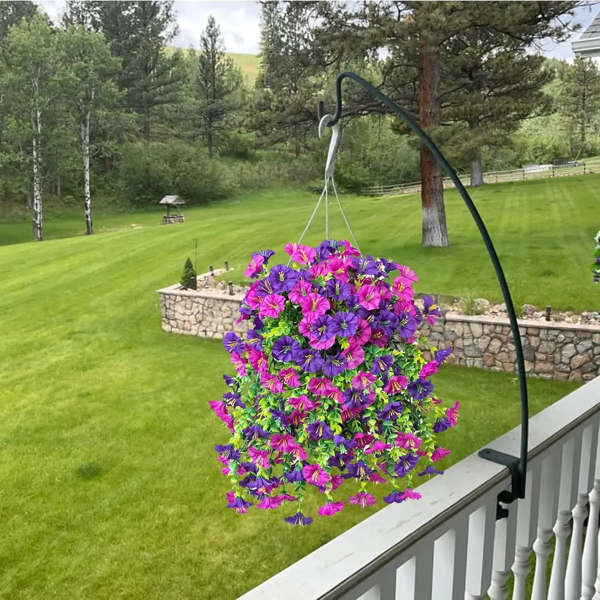 A purple morning glory and eucalyptus garland hangs from a curved metal wire on a white railing in a grassy yard.