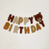 A banner spelling out Happy Birthday made of wooden letters and a teddy bear cutout.
