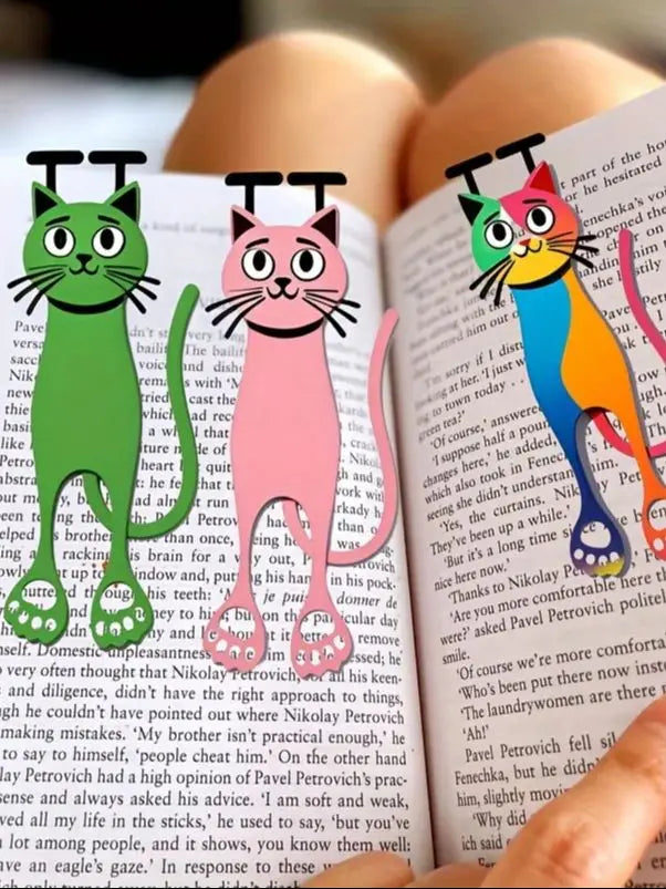 A close-up of a book featuring illustrations of three cats used as decorative bookmarks.