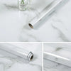 A silver roll of self-adhesive marble contact paper lying on a white marble surface.