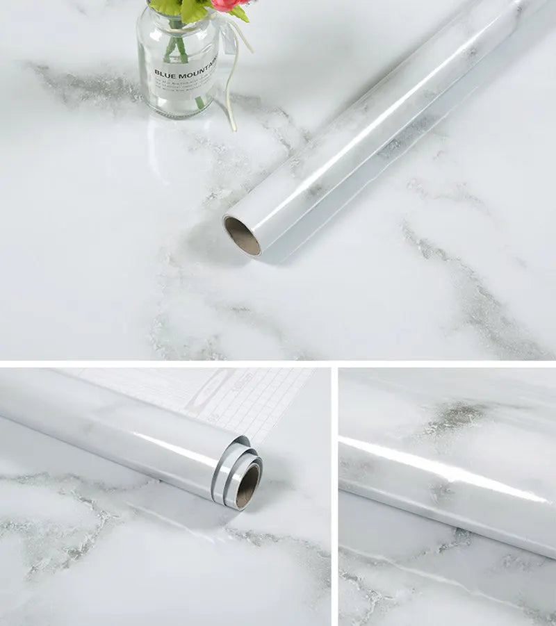 A silver roll of self-adhesive marble contact paper lying on a white marble surface.