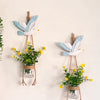 A decorative hanging display featuring white and blue bird-like figures with small potted yellow flowers.