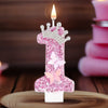 A pink glitter birthday candle shaped like the number one with a butterfly detail, lit on a wooden surface.