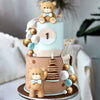 A tiered cake featuring a bear topper and decorative balls in brown, gold, and light blue tones.