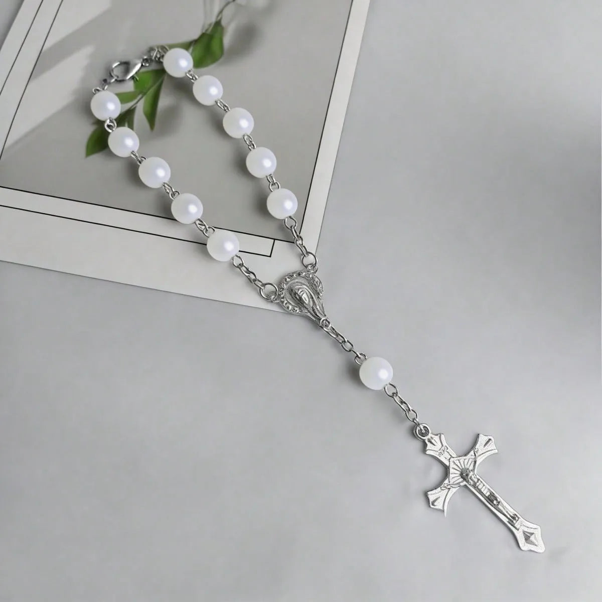 Silver rosary set featuring white pearl beads and a cross pendant on a light gray background.