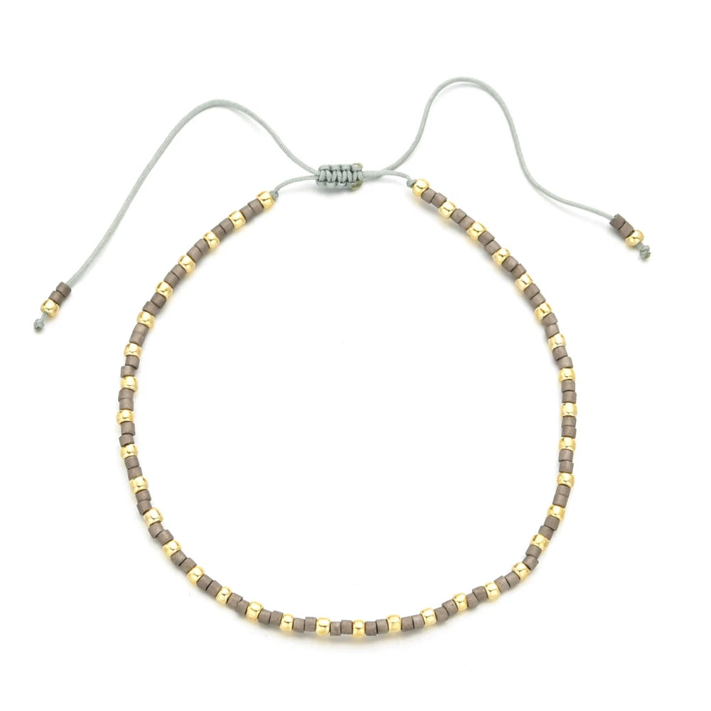 Handmade boho glass bead bracelet with an adjustable cord featuring small gold and gray beads.
