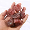 A hand holds several reddish-pink natural raw healing crystal stones for chakra balancing and home decor.