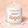 A white candle in a glass jar with a custom logo label, resting on pink petals.