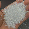A hand holds a pile of clear and iridescent multicolor AB glass micro beads for nail art and DIY crafts.