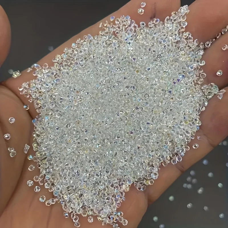 A hand holds a pile of clear and iridescent multicolor AB glass micro beads for nail art and DIY crafts.
