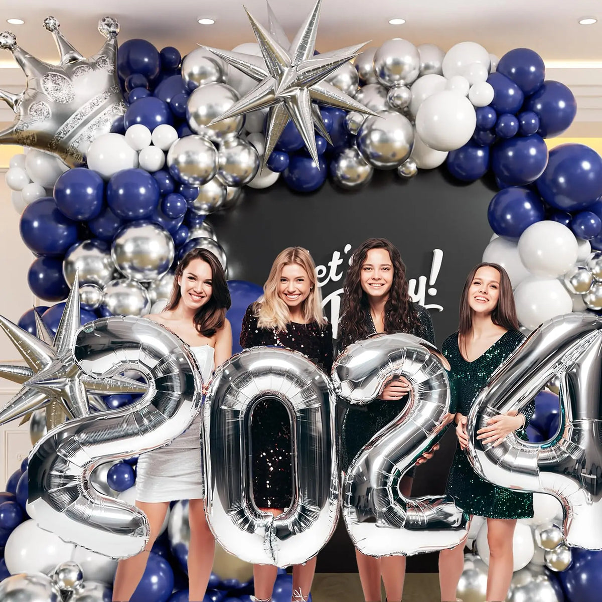 A balloon garland arch featuring navy blue and silver balloons decorated with a crown and star, alongside three smiling women