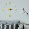 A modern wall clock with gold numbers and hands is displayed above a gray sofa.