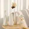 A collection of white ceramic bud vases and a dried flower displayed on a wooden surface.