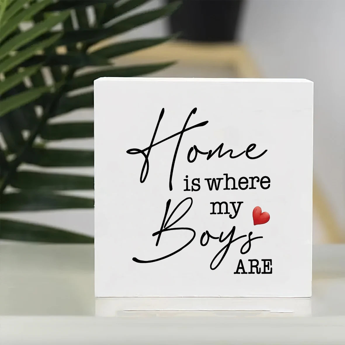 A white sign with black script that reads Home is where my Boys are and a small red heart.