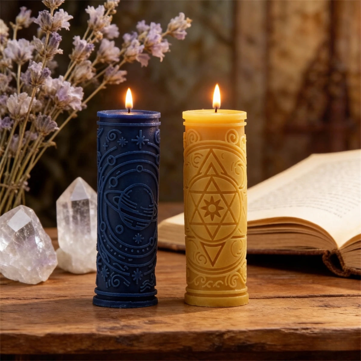 Two glowing candles in blue and yellow holders sit on a wooden surface next to a book and lavender flowers.