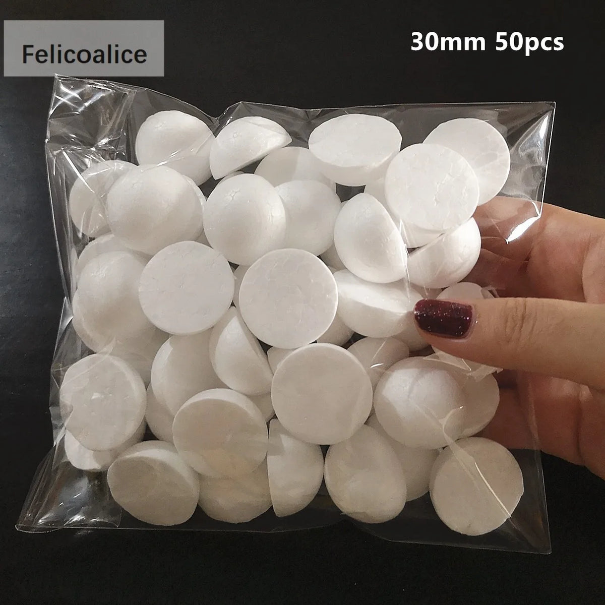 A hand holds a clear plastic bag filled with 50 white polystyrene foam balls for crafting.