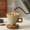 A ceramic coffee mug with a wooden base is being filled by a pour-over device, creating steam.