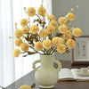 A bouquet of yellow silk chrysanthemum artificial flowers in a white vase on a wooden table.