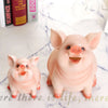 A cute pink resin piggy bank with a smiling expression sitting on a white surface.