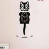 A black cartoon cat wall clock featuring a face and a swinging tail, displayed against a light pink wall.