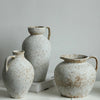 A pair of speckled, light ceramic vases with handles are displayed against a plain gray background.