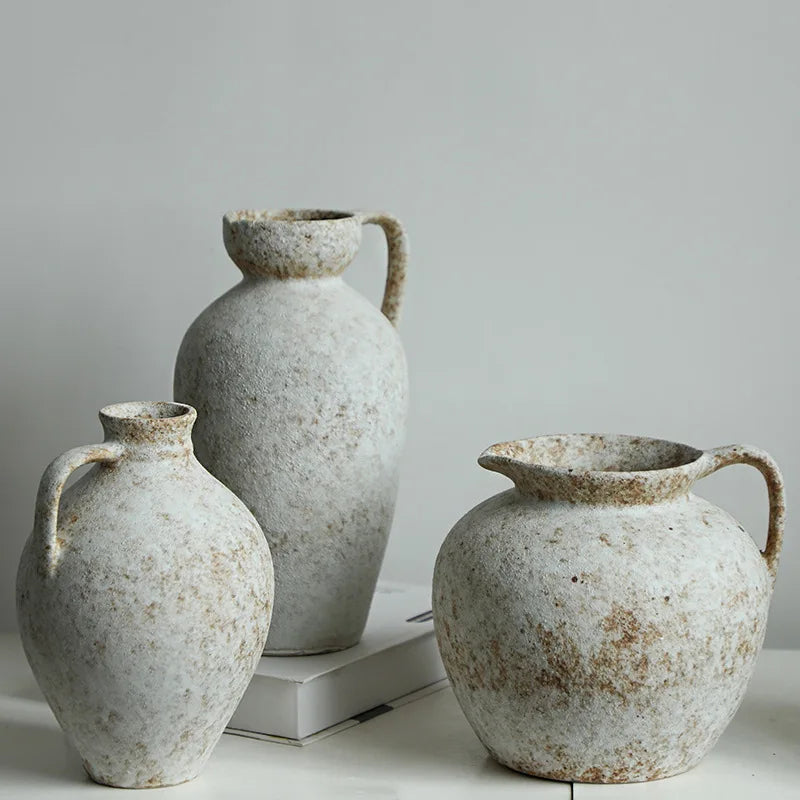 A pair of speckled, light ceramic vases with handles are displayed against a plain gray background.