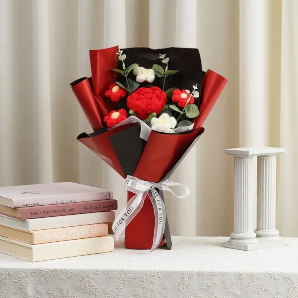 A bouquet of red and white crochet rose flowers wrapped in dark red paper and tied with a white ribbon.