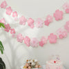 Pink cherry blossom paper flag banner hanging against a white wall with a cake in the foreground