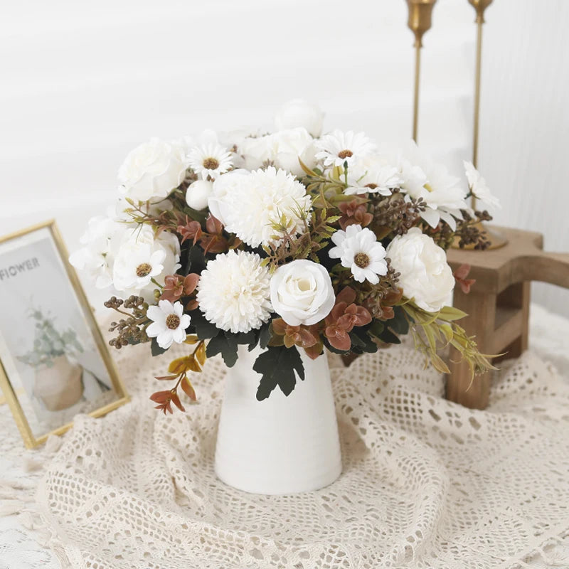 A white floral bouquet featuring white and cream flowers and dried foliage in a ceramic vase on a lace cloth.
