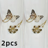 A set of two decorative flower butterfly curtain tiebacks with gold accents against a white fabric background.