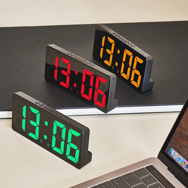 Three digital alarm clocks displaying 13:06, with two black and one green model resting on a dark surface.