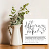 A white ceramic pitcher holds green foliage, next to a sign defining a difference maker.