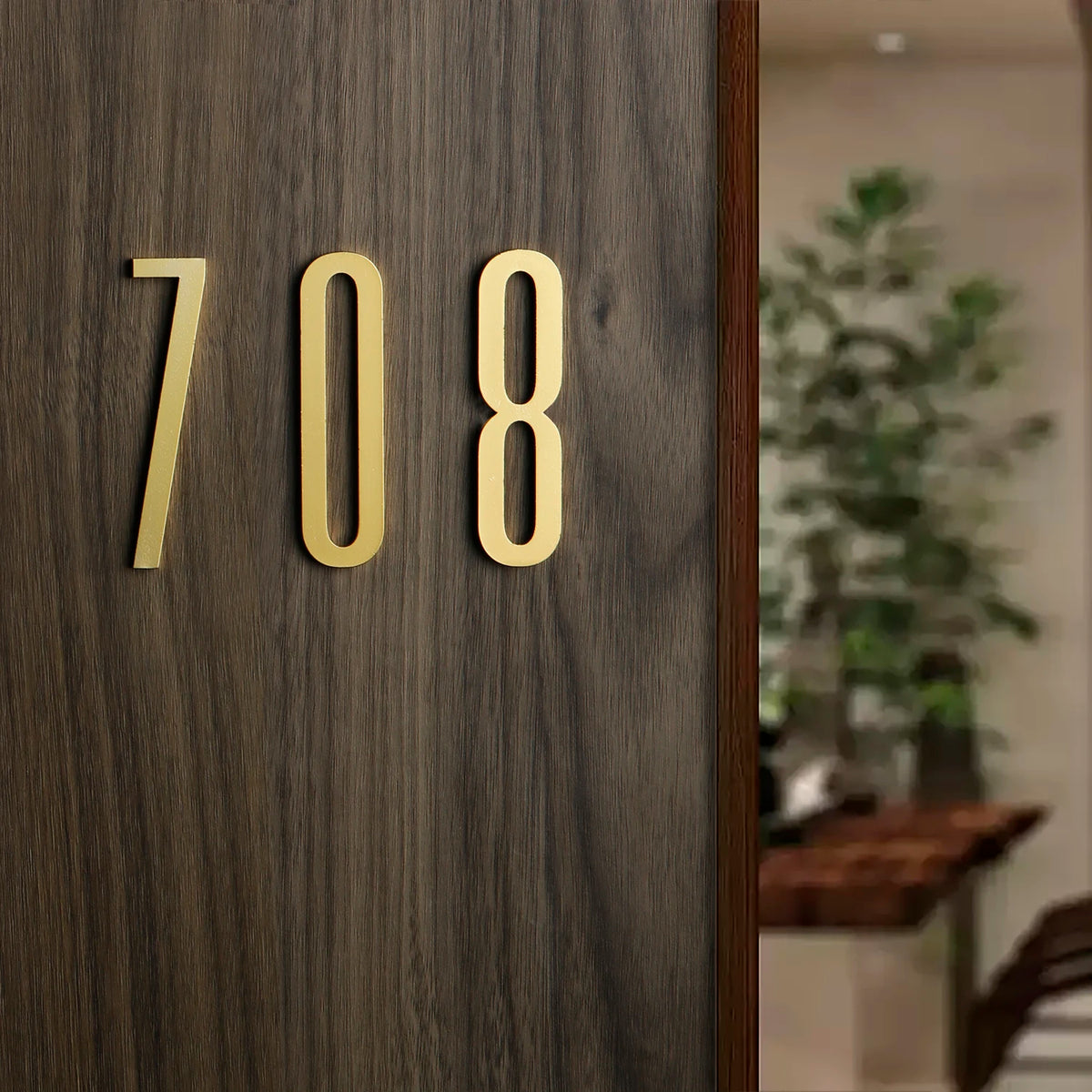 Close-up of a polished gold house number 708 mounted on dark wood paneling.