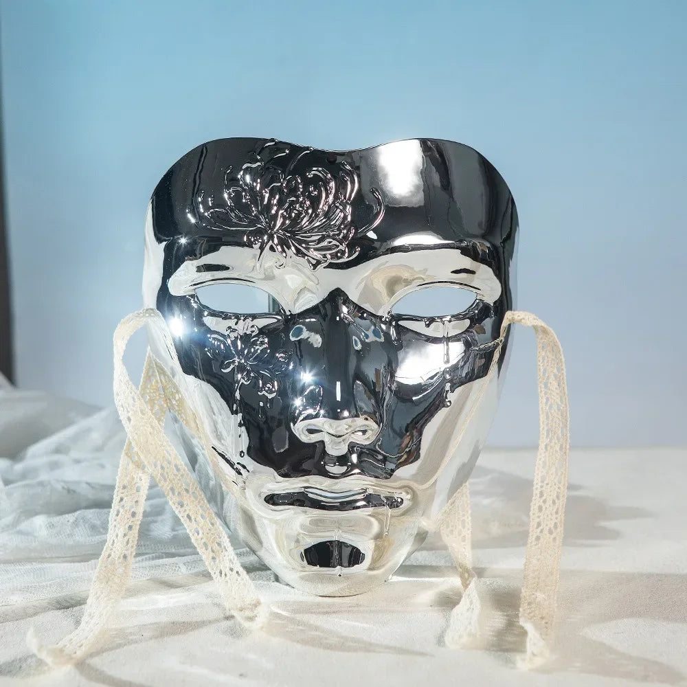 A silver masquerade mask with intricate floral patterns and a Hanfu-inspired design displayed on white fabric.