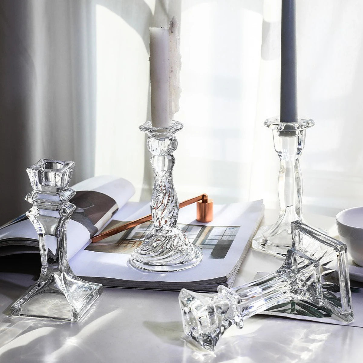 Elegant clear glass pillar candle holders displayed on a white surface next to a lit candle.