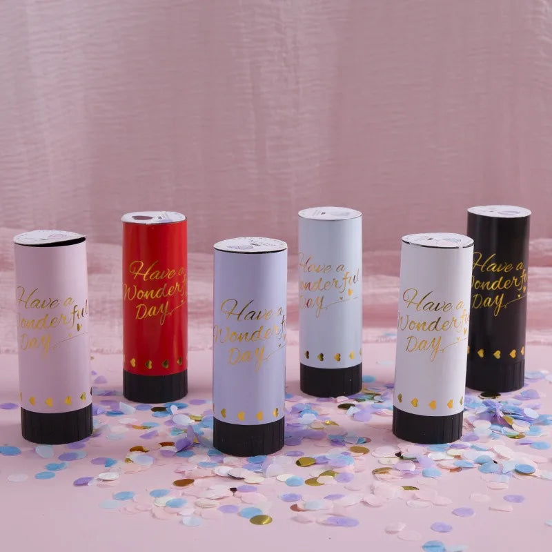 A set of hand twist confetti cannons in white and red colors displayed on a pink surface.