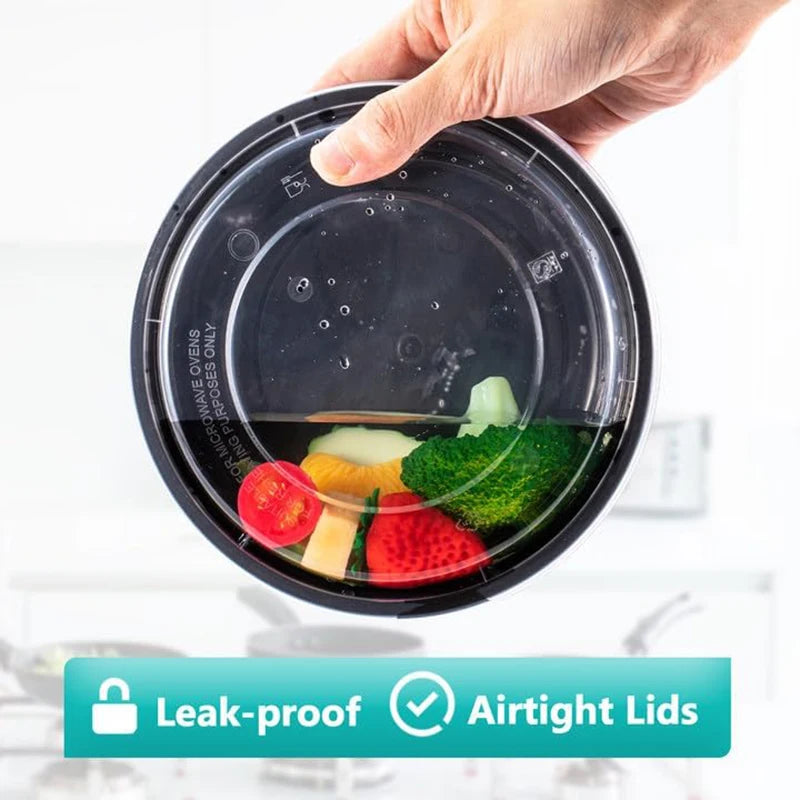 A hand is holding a round, black meal prep container with an airtight lid, showing fresh vegetables inside.