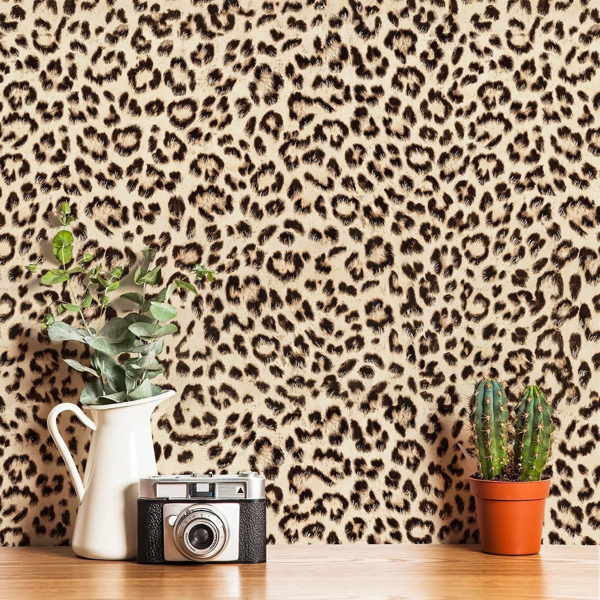 A close-up of a wooden surface featuring a retro leopard print wallpaper, a white pitcher, and a vintage camera.