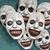 A collection of white demon masks with painted features and red teeth displayed on a green grid.