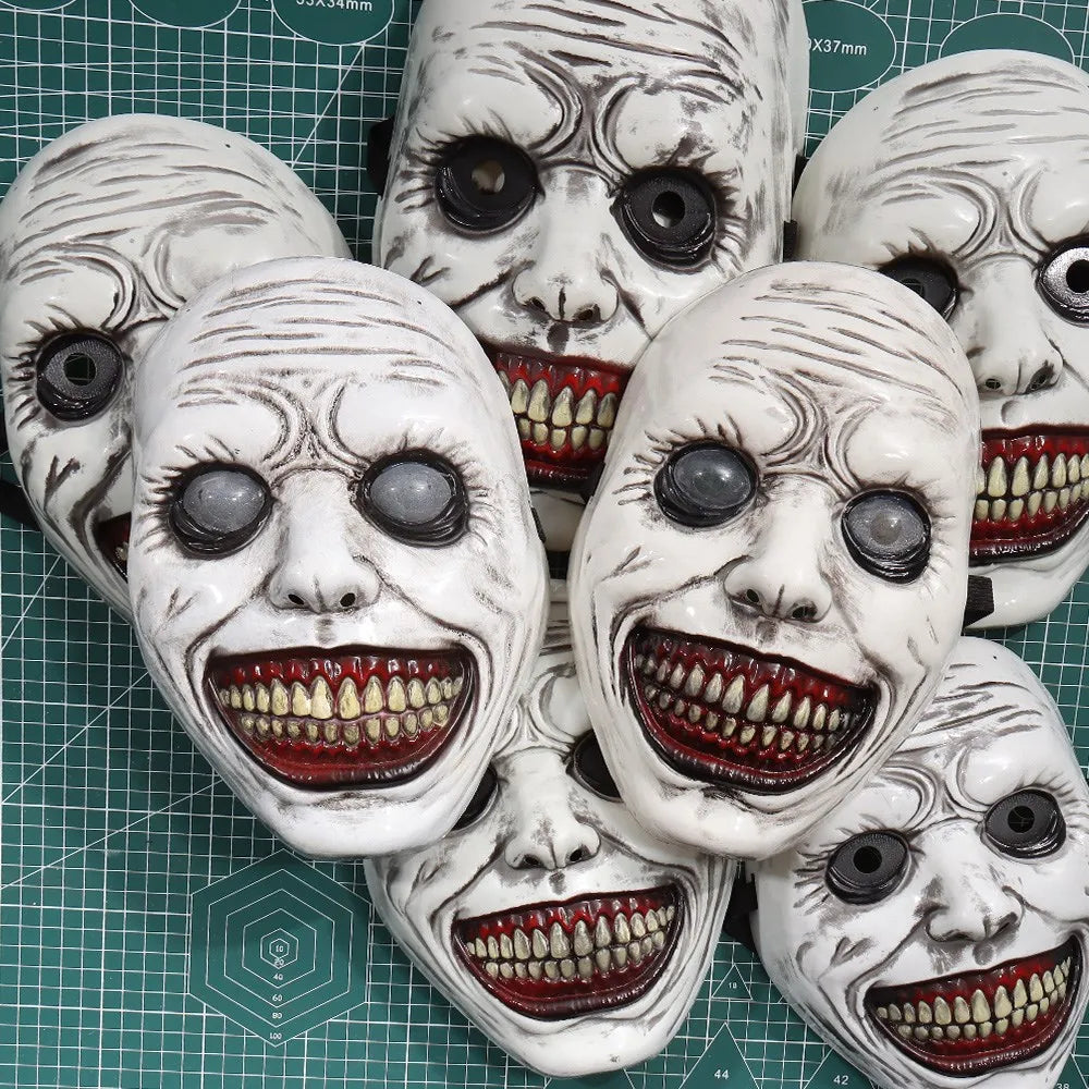 A collection of white demon masks with painted features and red teeth displayed on a green grid.
