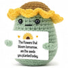 A handcrafted crochet animal doll with yellow hair and green body holding a card that reads The flowers that bloom tomorrow a