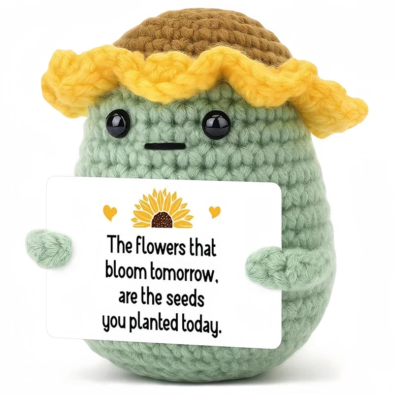 A handcrafted crochet animal doll with yellow hair and green body holding a card that reads The flowers that bloom tomorrow a
