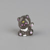 A small, dark gray resin keychain of a cat with pink and yellow markings and white paws.
