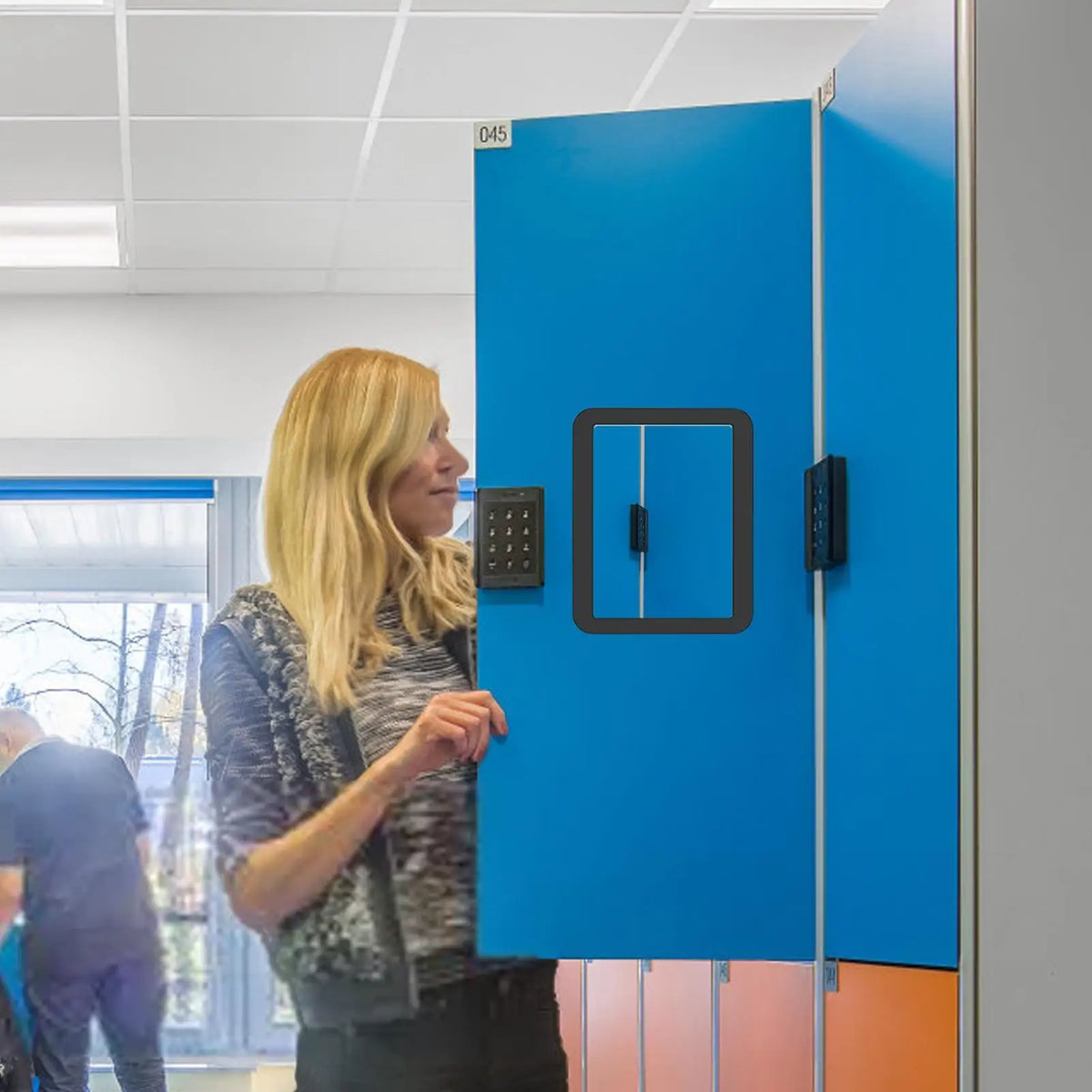 A woman is interacting with a bright blue magnetic locker door, which features an access panel.