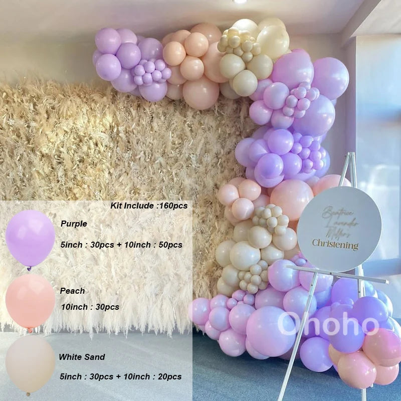 A balloon garland kit featuring purple, peach, and white balloons arranged against a fluffy beige backdrop.