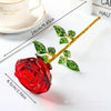 A bright red crystal glass rose flower branch with green leaves displayed on a white surface.