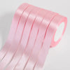 Pink silk satin ribbons rolled and stacked, showing a smooth texture and vibrant color.