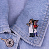An enamel pin featuring two cartoon characters dressed as burgers on a denim shirt.