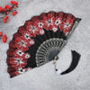 A black folding fan decorated with red and white floral patterns on a gray background.