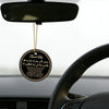 A round gold prayer tag with Arabic and English text hangs from a black light fixture above a car steering wheel.